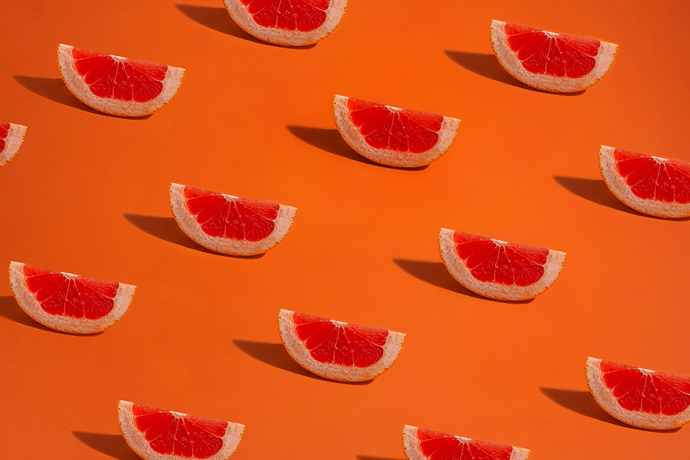 Lot de pamplemousses vue d'en haut séparées les uns des autres de manière équidistante avec une ombre portée à gauche. Image de estudio-bloom-tOitjphtIXU-unsplash